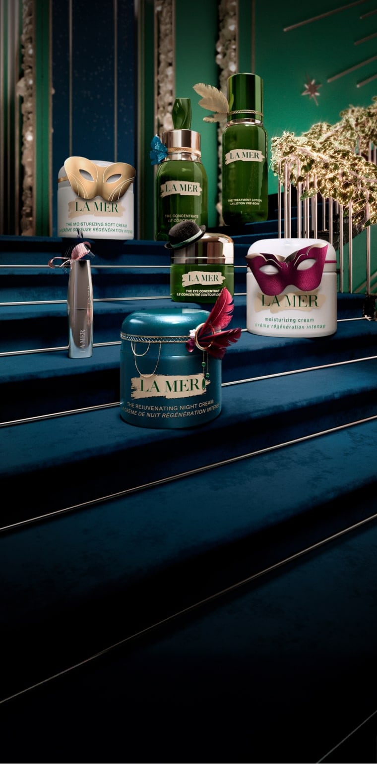 Selection of bestselling La Mer products placed on a festive, grand staircase, decorated in miniature masquerades and headwear