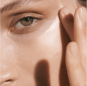 Close up of model applying Crème de la Mer to cheek, in bright, ambient lighting