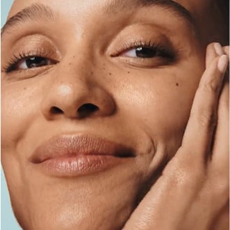 Close up of model applying serum to cheek, smiling