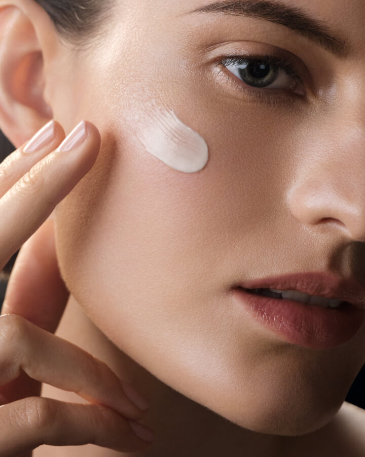 Close up photograph of woman applying the rejuvenating cream on her cheek bone.