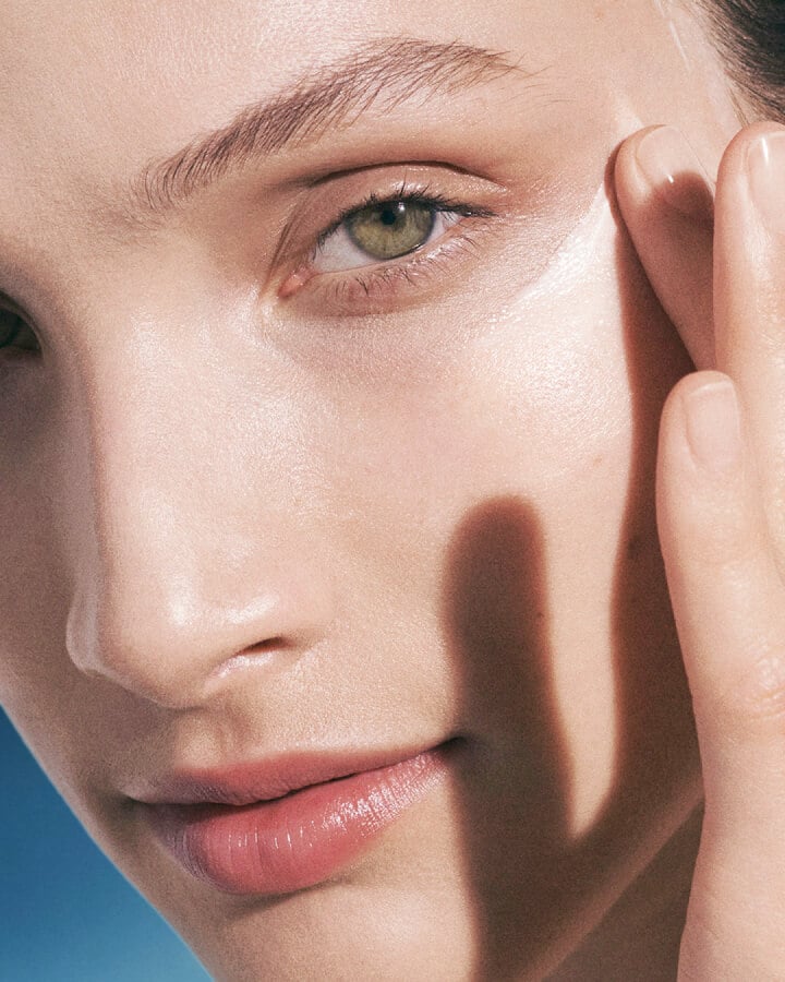 Close up photograph of woman applying moisturising soft cream to her cheek bone.