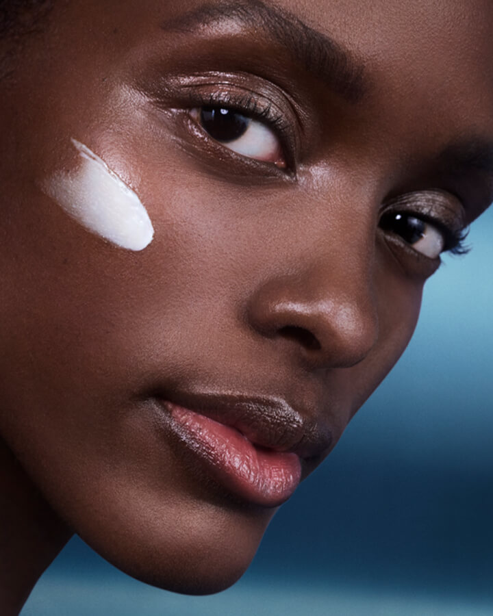 Close up photograph of woman with a smear of creme de la mer cream on her cheek bone.