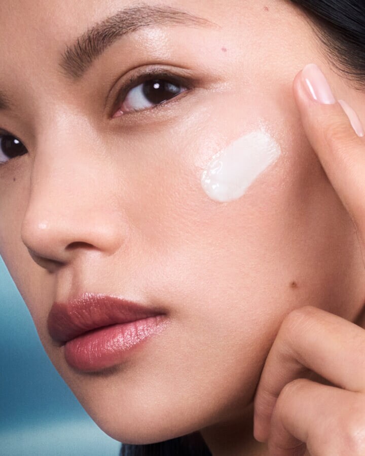 Close up photograph of woman applying La Mer moisturizing fresh cream.